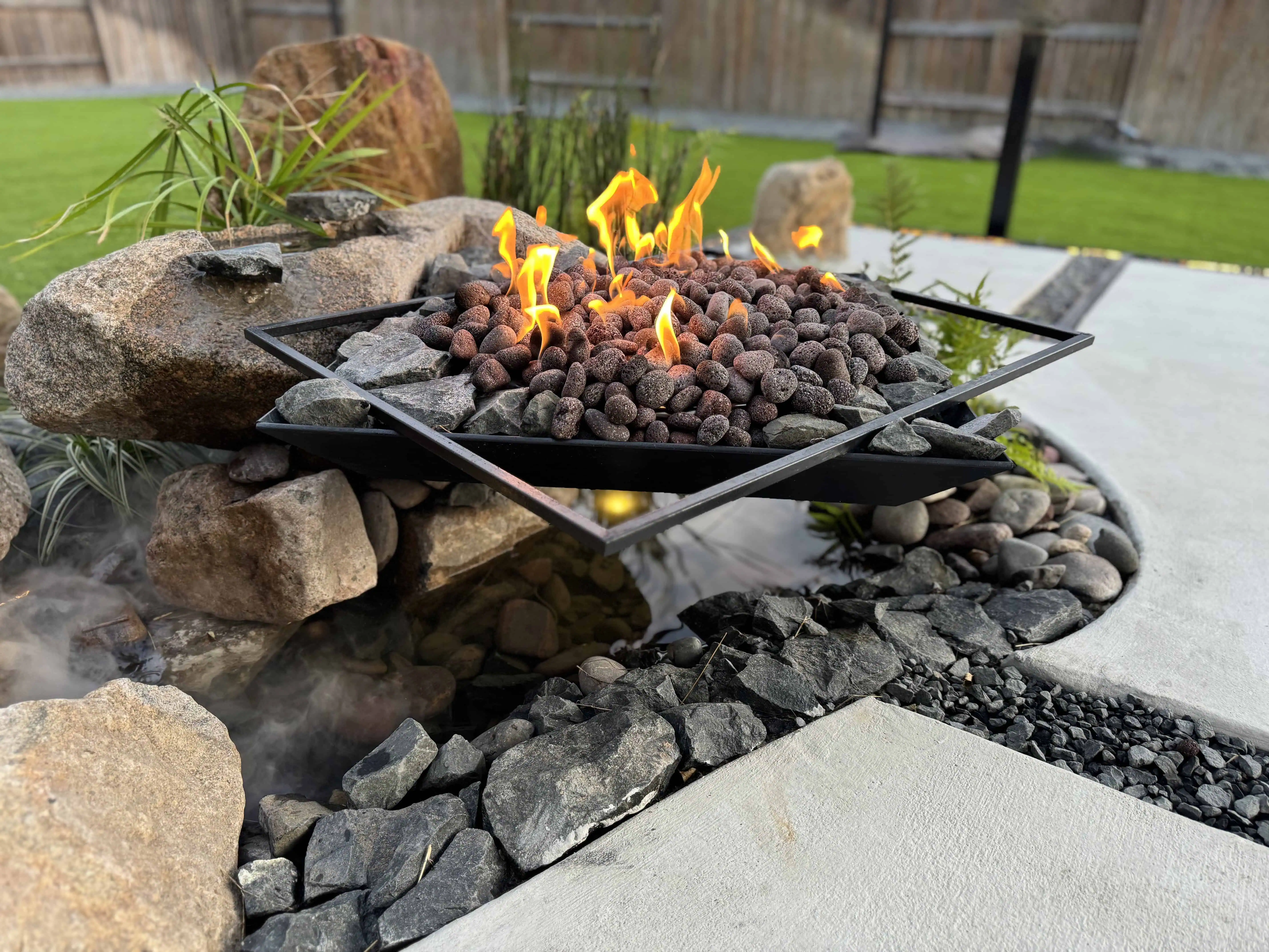 Diamond-oriented floating fire pit with rounded volcanic rock and boulder fountains — Pflugerville TX