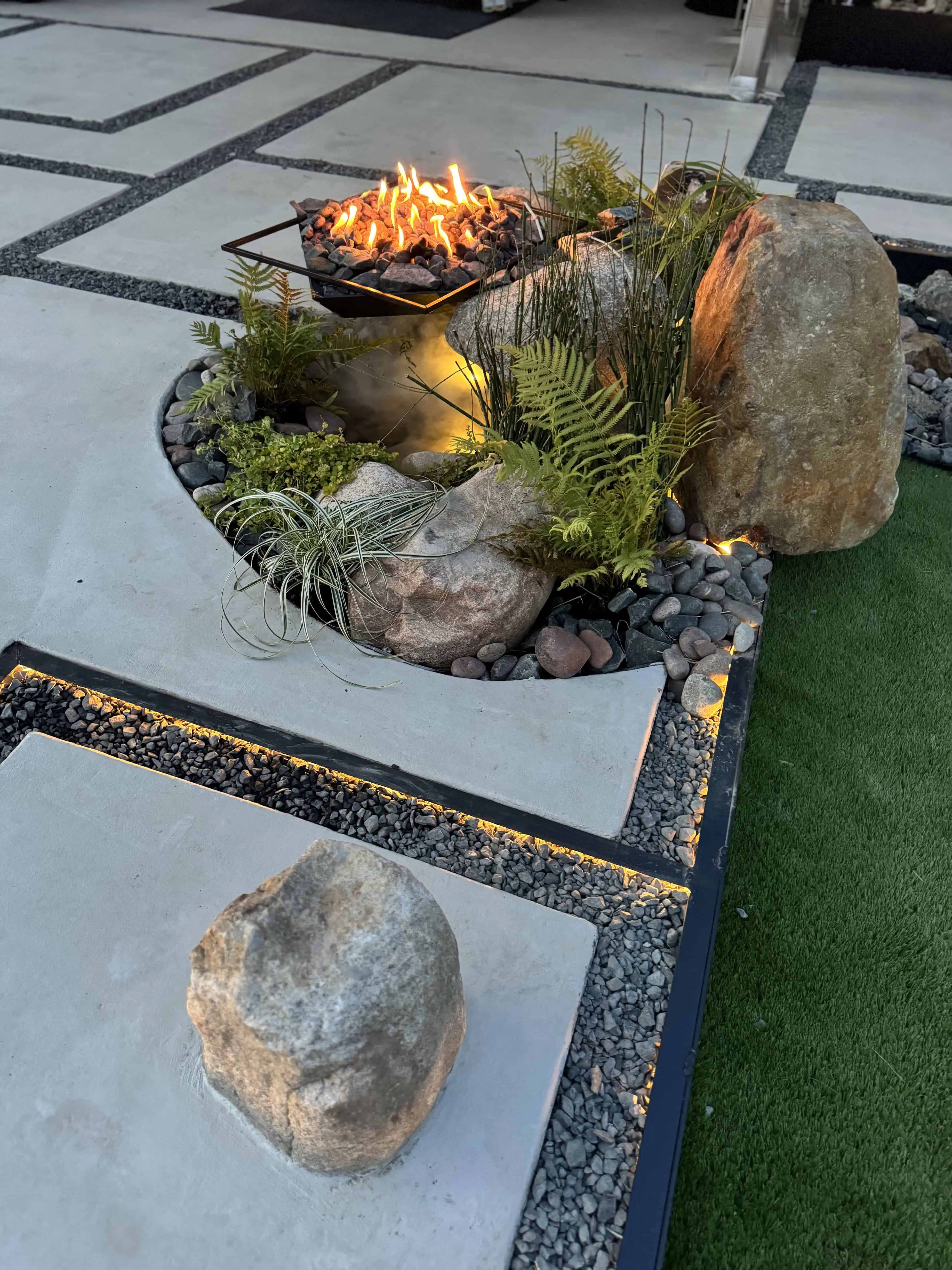 Full composition — fire pit, boulder fountains, COB-lit pavers, fern planting beds — Pflugerville TX