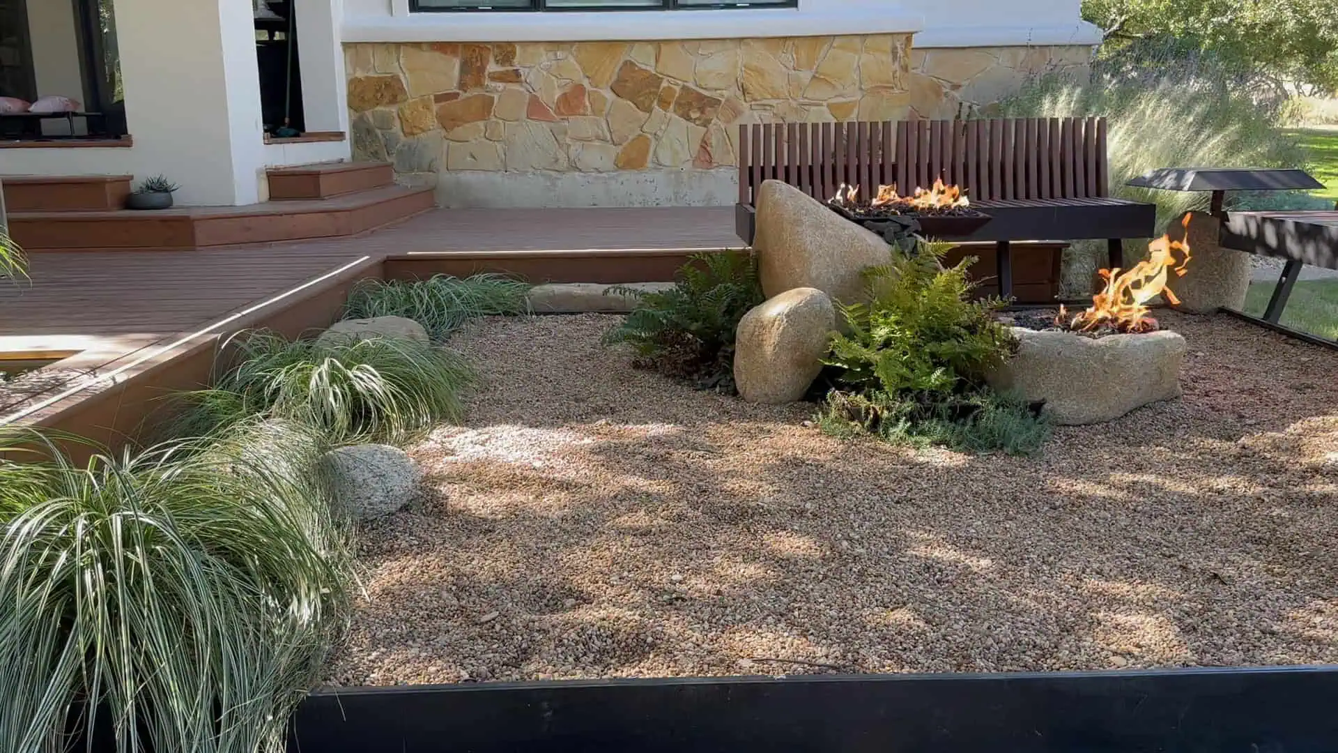 Stone fire pit area with timber benches, boulders, grasses, and deck — Circle C Austin TX