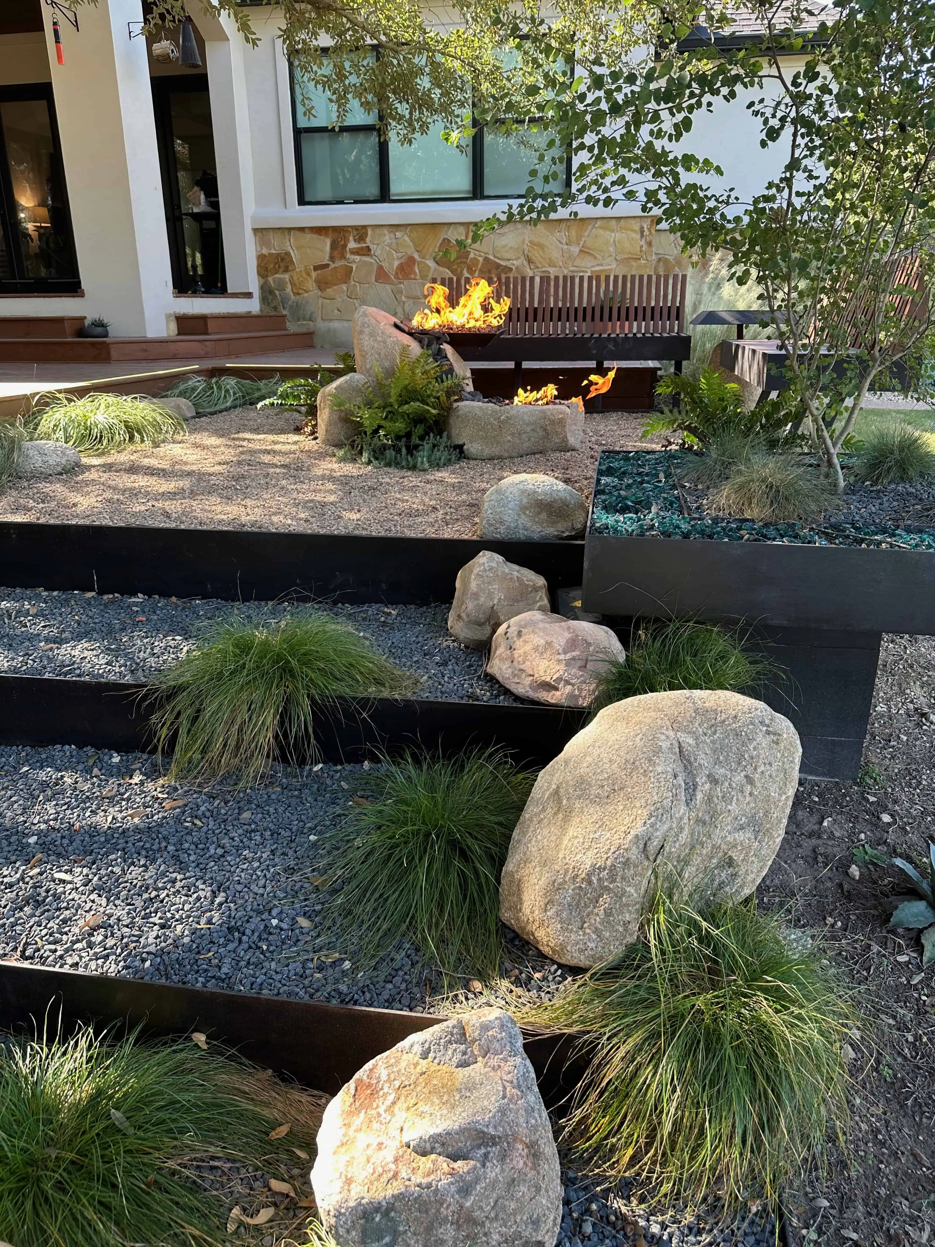 Three terraced steel areas with boulders and ornamental grasses stepping down from the house — Circle C Austin TX
