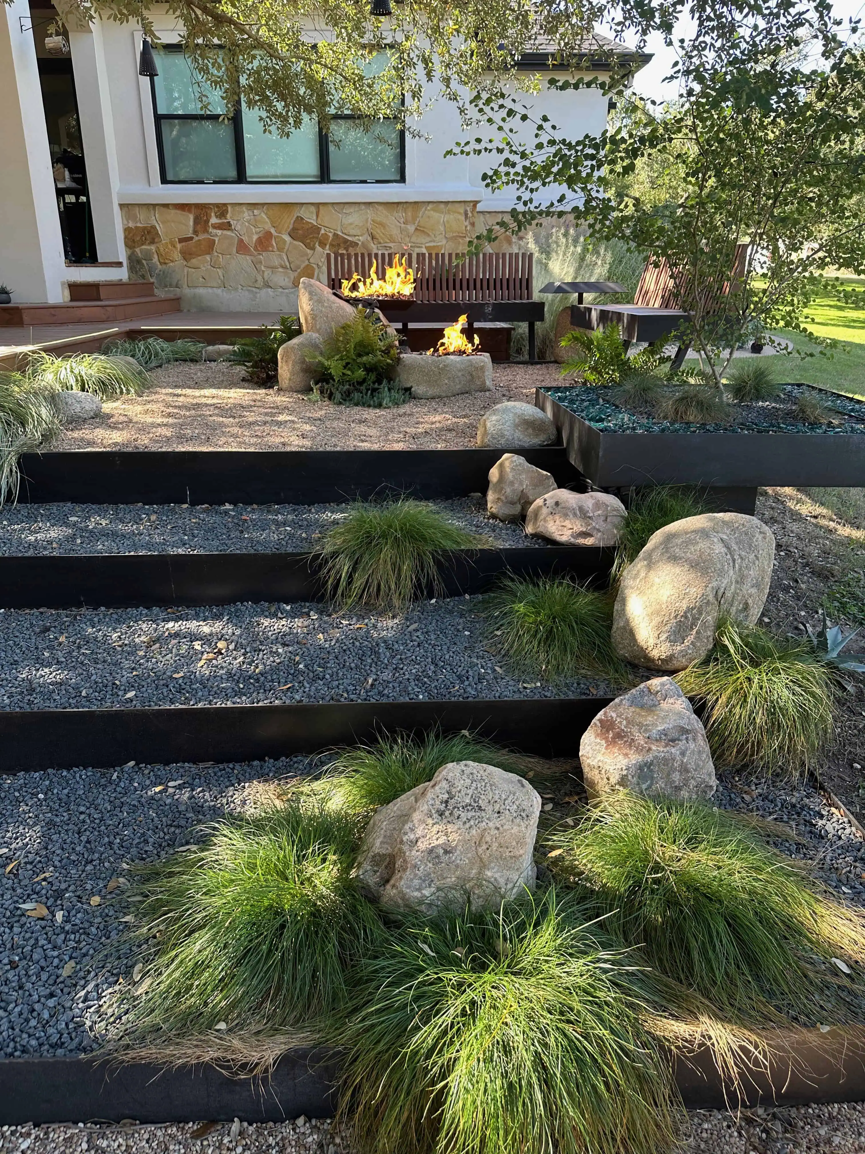 Full view — three terraced steel areas with boulders, grasses, and stone fire pit — Circle C Austin TX