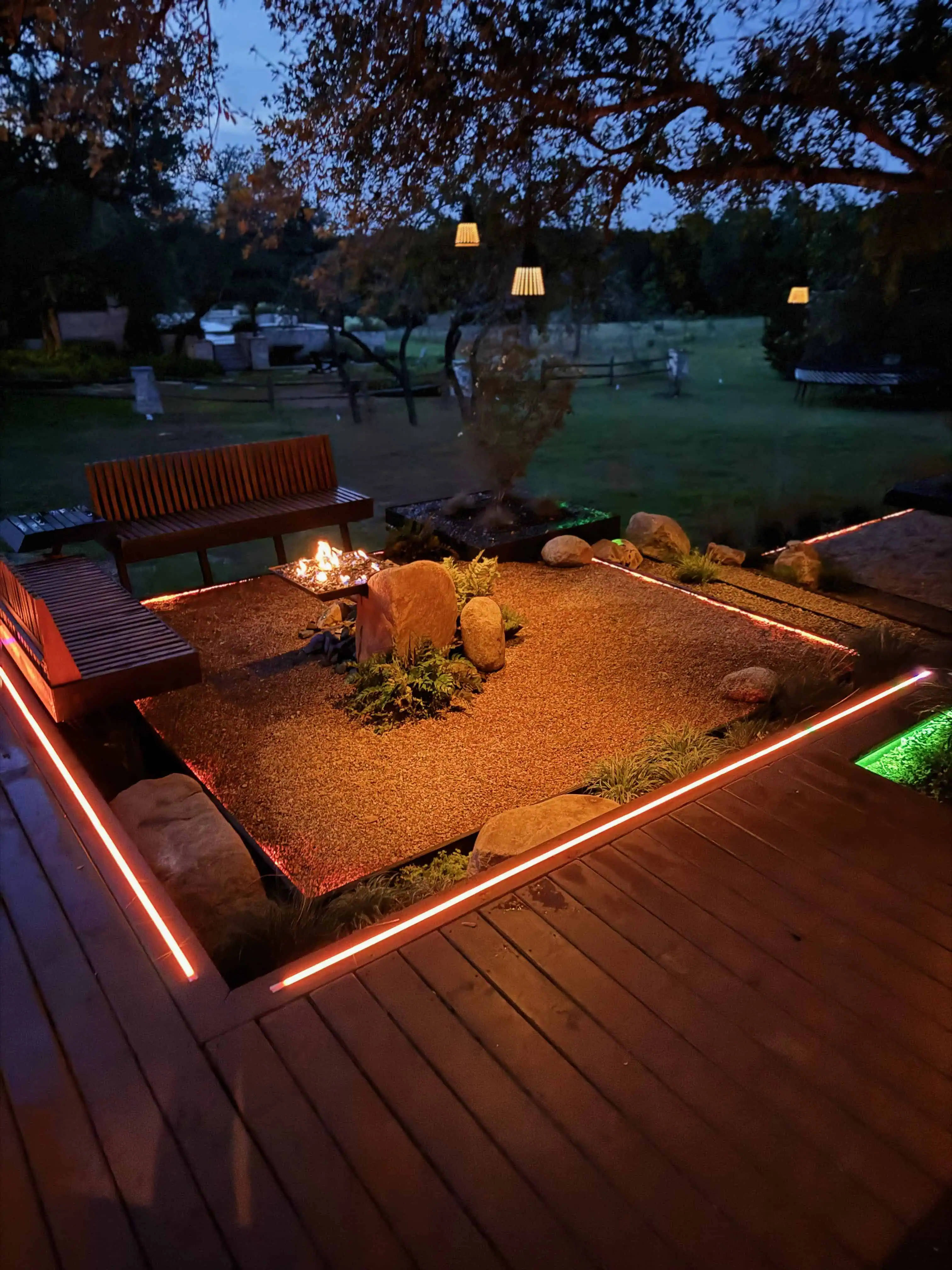 Night fire pit — hanging lanterns, bench seating, amber deck lighting — Circle C Austin TX