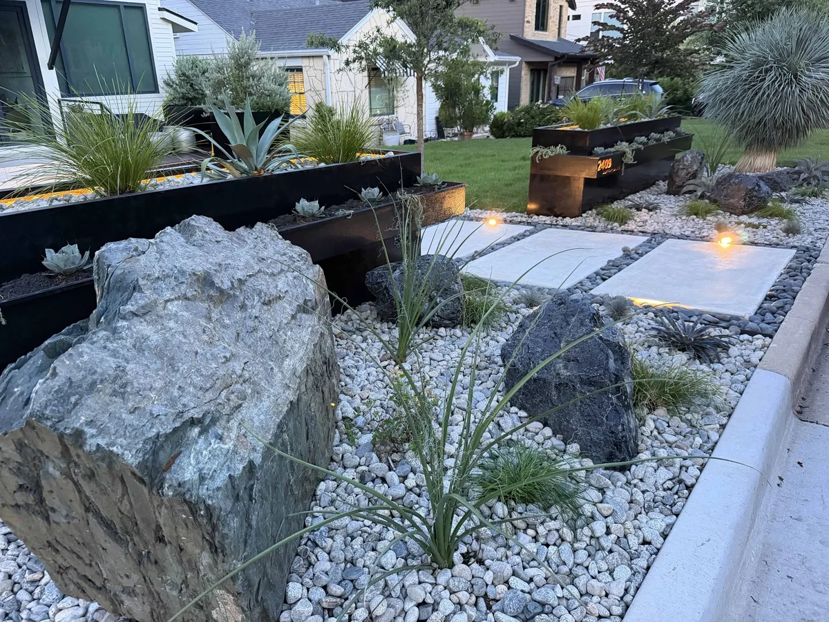 Full front yard view — cantilevered steel planters, boulders, concrete stepping stones, native planting, COB lighting — Tarrytown Austin TX