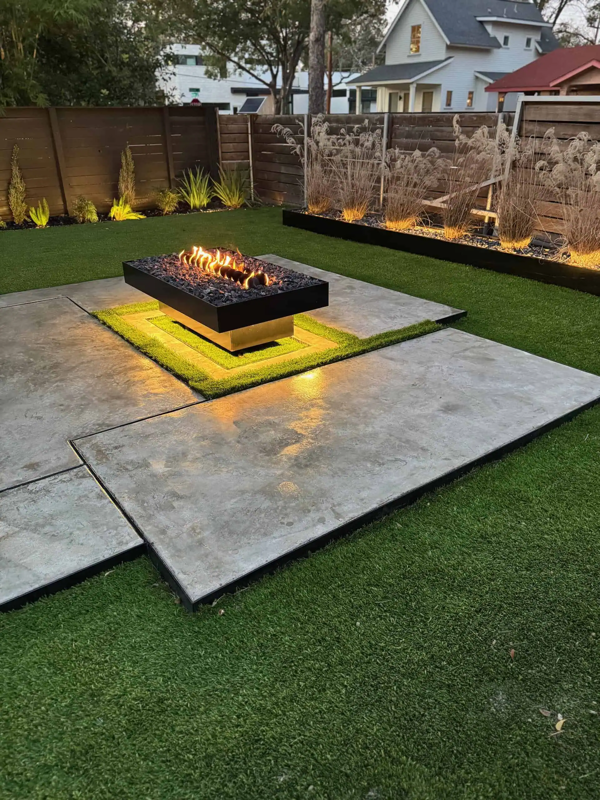 Evening — concrete slabs, fire pit glowing, planting beds lit — Austin TX